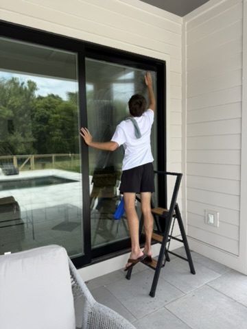 Technician detailing a tall sliding glass door on a covered porch